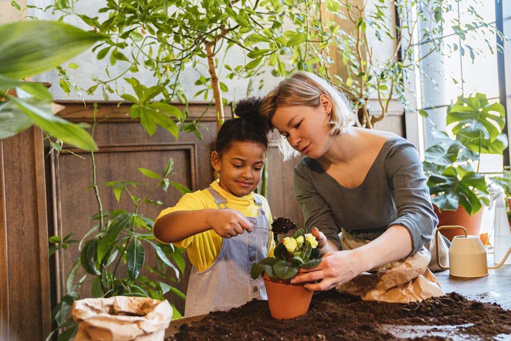 A woman and child bonding over indoor gardening, planting a flower in a clay pot.