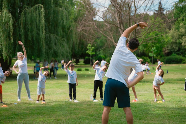 Children and instructors stretching in a park during a summer physical education class.